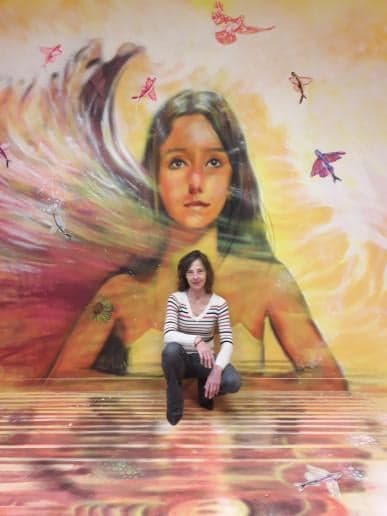 Diane assise devant sa fresque L’Éveil, qui donne l’échelle du mur